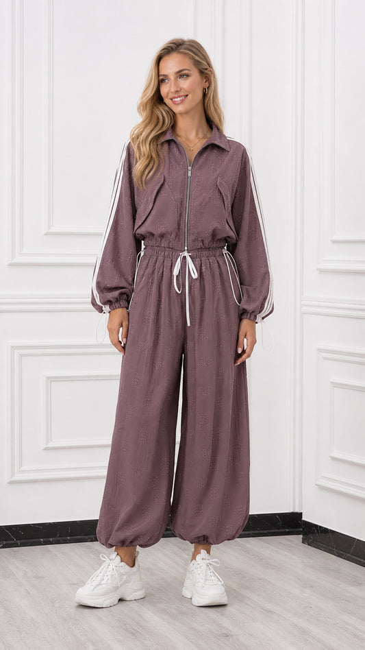 Front view of woman wearing a mauve long sleeve zip-up track jumpsuit with white side stripes